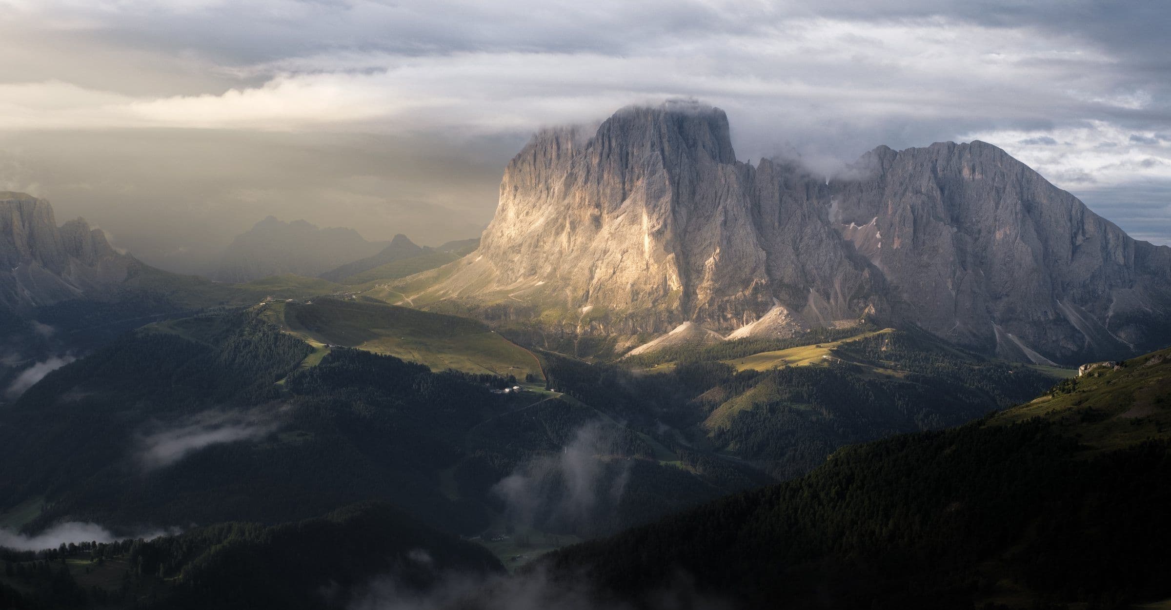 Light breaking over the Langkofel massif above misty forests